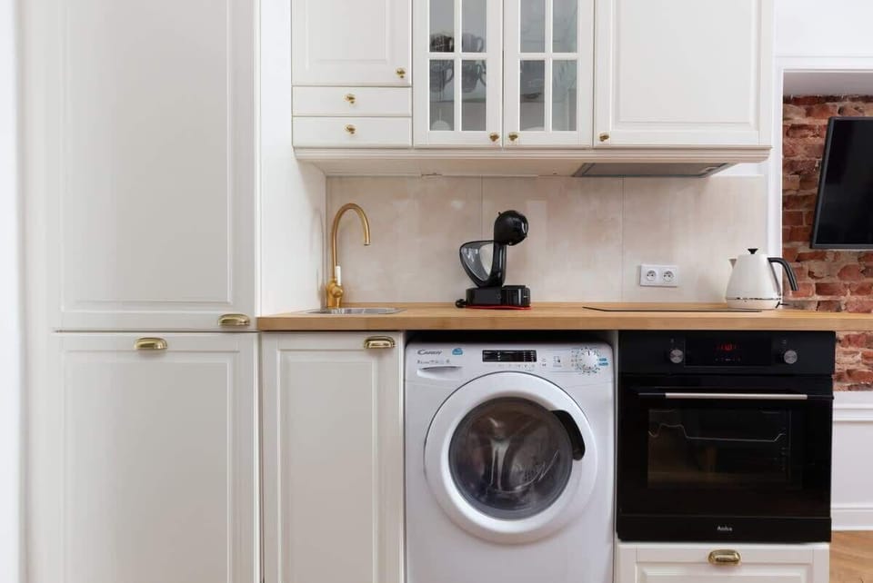 A photo fully showing off a unique kitchen with beautiful, stylish furniture and appliances such as a washing machine, oven, hob, built-in fridge and cooktop.