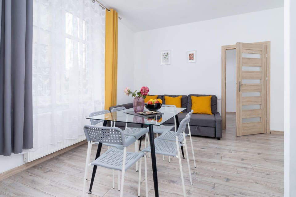 A dining area featuring a table with chairs and bright natural light from a large window with white curtains.