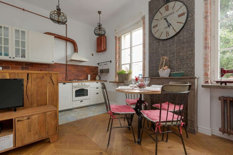 A stylish open-concept kitchen featuring a combination of white cabinetry, exposed brick backsplash, and wooden countertops, blending modern and rustic styles.