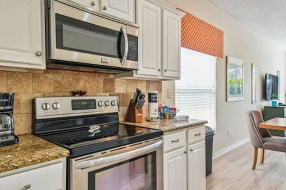 Enjoy cooking in this well-equipped kitchen with stainless steel appliances and beautiful granite countertops. Cheerful orange accents add brightness, while natural light from the window creates a warm, inviting atmosphere.
