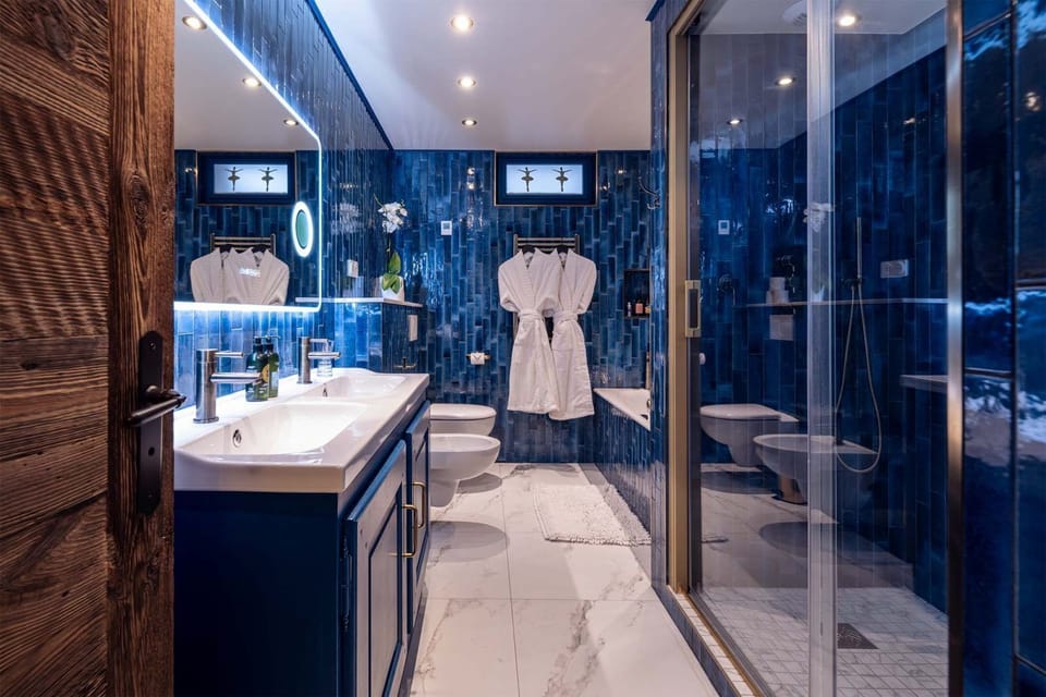 Bright bathroom with blue tiled walls, dual sinks, and a walk-in shower