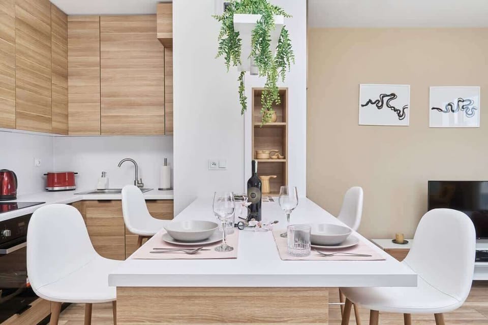 A stylish dining and kitchen area with wooden cabinetry, sleek white chairs, and greenery for a fresh touch.