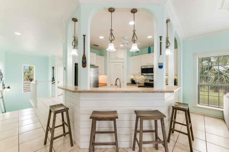 Step into your bright coastal kitchen where soothing mint walls and elegant pendant lighting create the perfect space for morning coffee or evening gatherings.