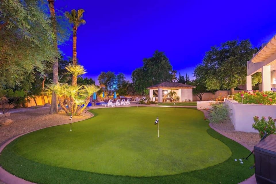 A lush private putting green awaits under twilight skies, surrounded by palm trees, desert landscaping, and inviting poolside seating—ideal for evening play and relaxation.
