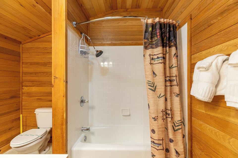 Rustic knotty pine bathroom with a charming fishing-themed curtain, ready to refresh the whole crew after a day in the mountains.
