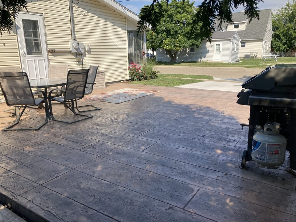 Stamped & colored patio with gas grill, wood burner and 6 chairs with table.