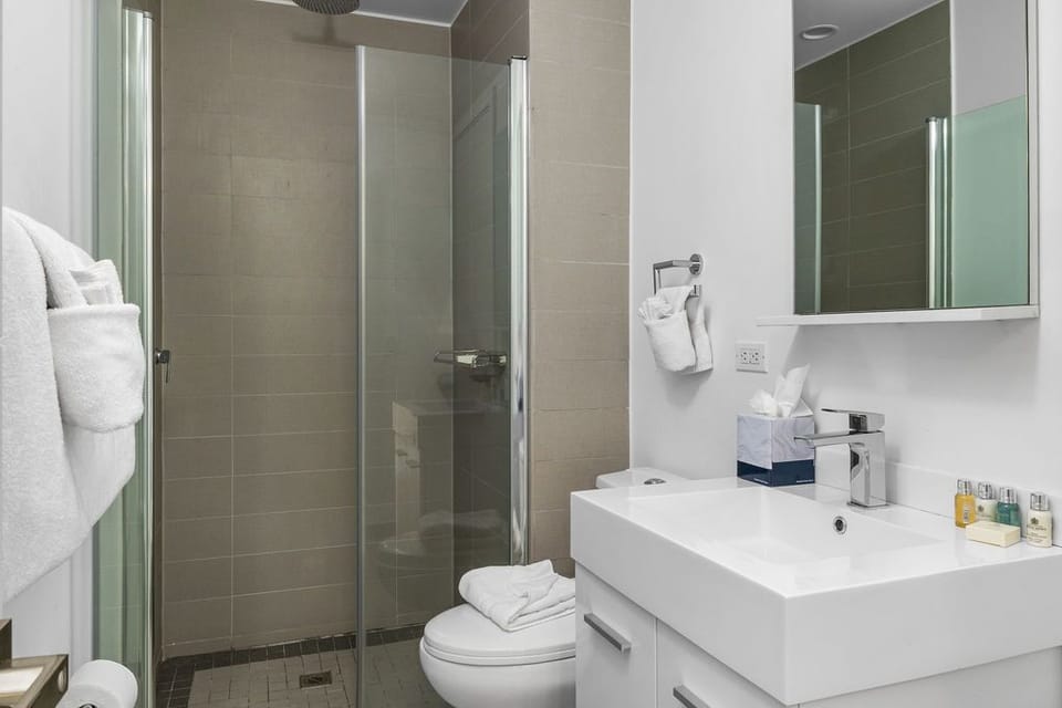 Your private bathroom offers a spacious walk-in shower with sleek tile, a modern vanity with fresh linens, and thoughtful amenities to refresh after your day of exploring.