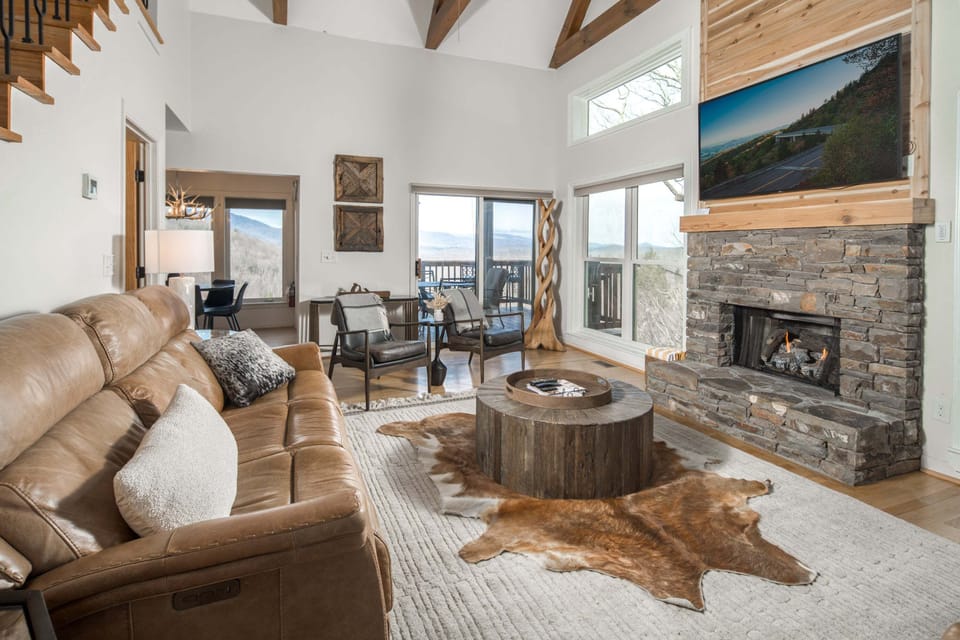 The bright, vaulted great room pairs cozy seating and a stone fireplace with mountain views front and center.