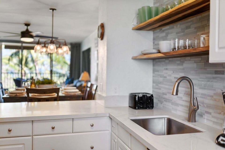 Open shelving, warm accents, and a sleek sink area create a clean and airy kitchen space.