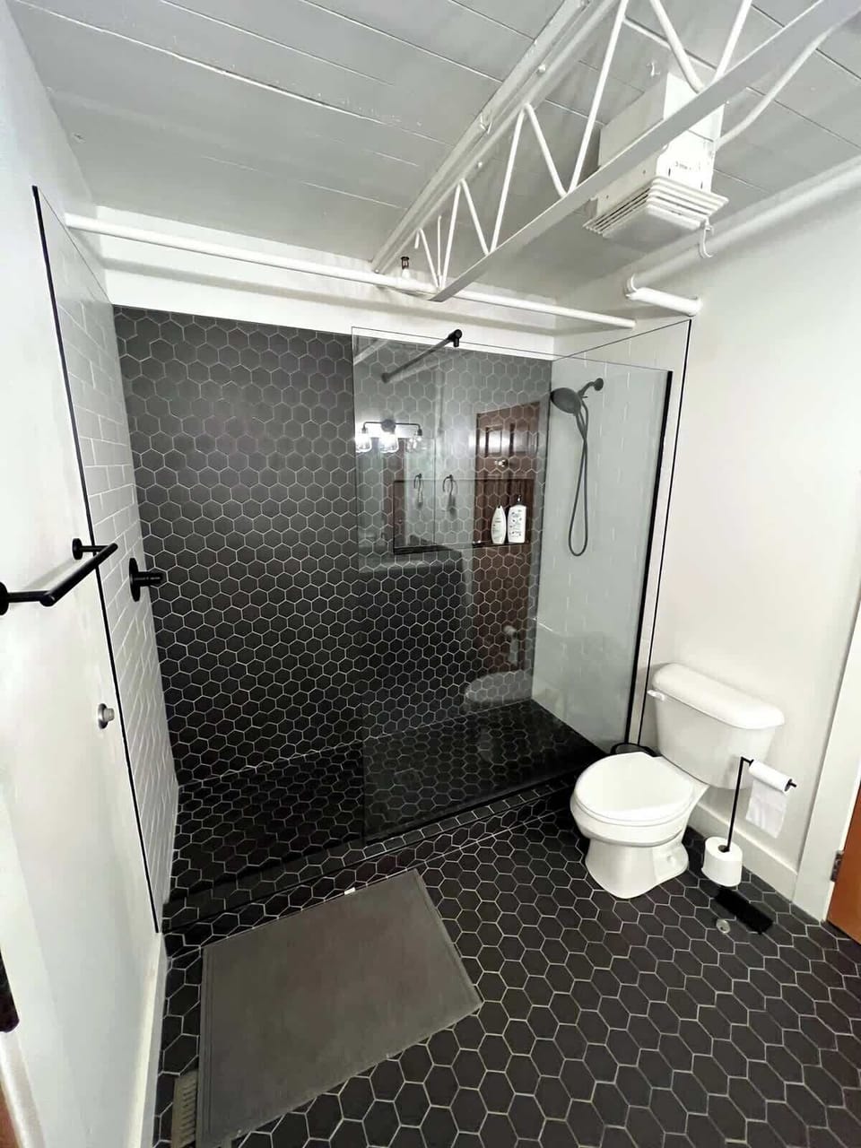 Walk in shower tiled in black hex with a glass surround.