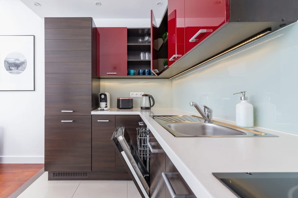 A modern kitchenette with a bright red backsplash, dark cabinets, and stainless steel appliances.