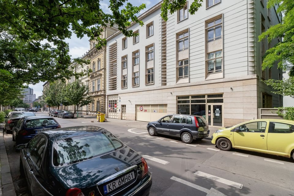 A street view with parked cars and a classic city building in the background. The area appears to be a central urban location.