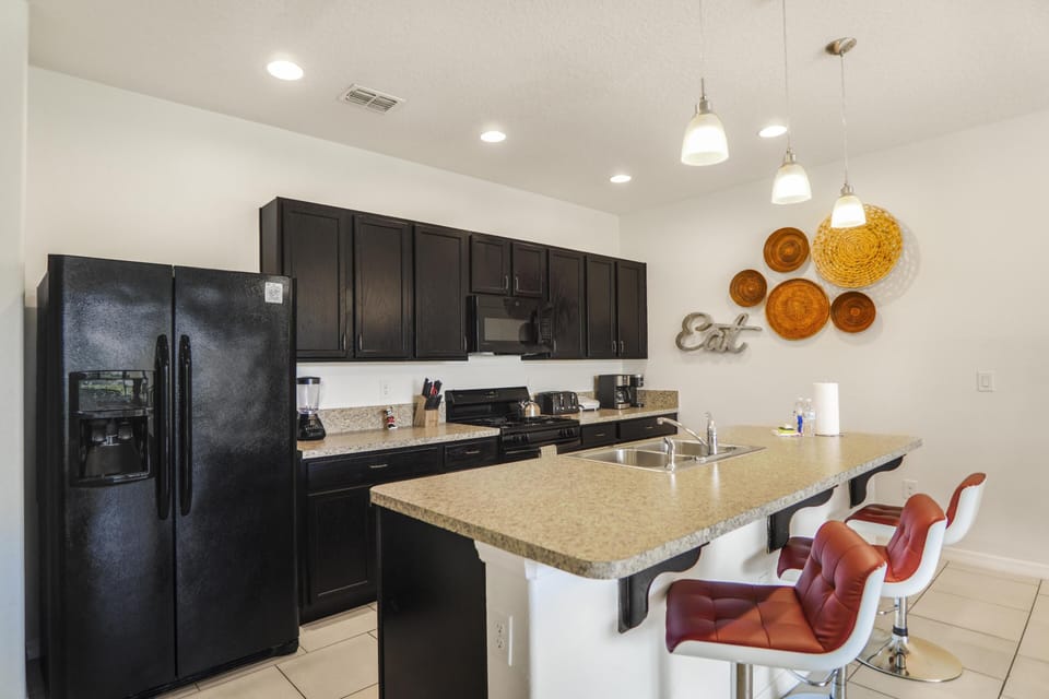 Black appliances and cabinetry contrast with beige granite countertops and red cushioned bar stools at the kitchen island.