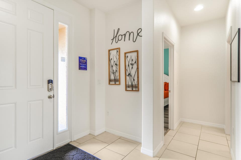 Entryway with white tile flooring, a white front door featuring a vertical window, and metal bird wall art under "Home" script.