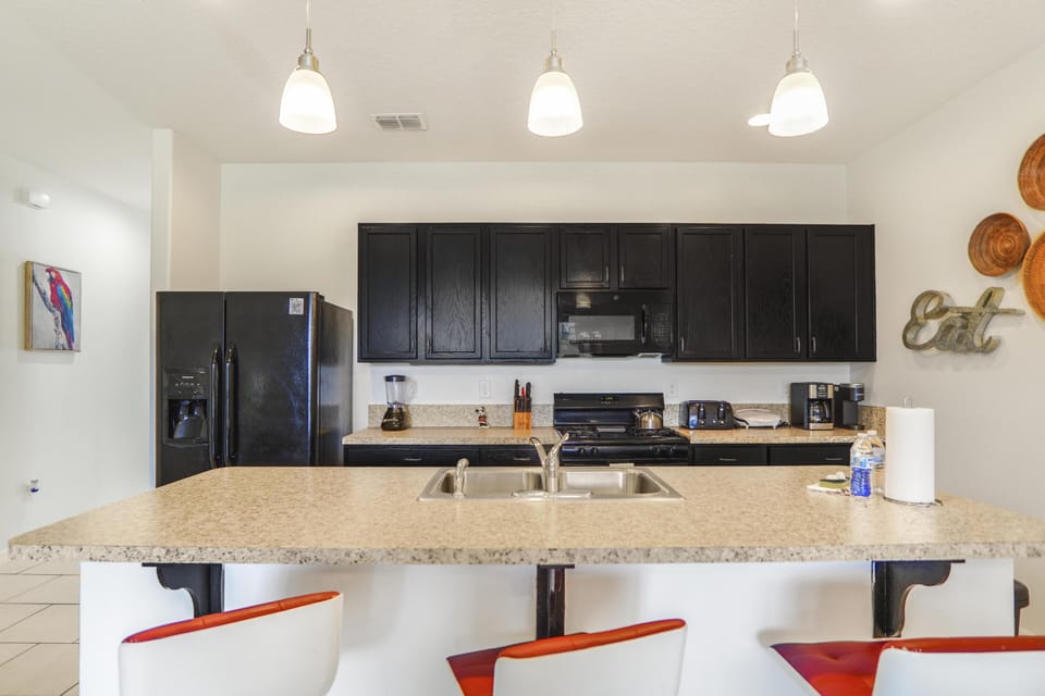 Black cabinetry and appliances line the kitchen wall above granite countertops illuminated by three pendant lights.