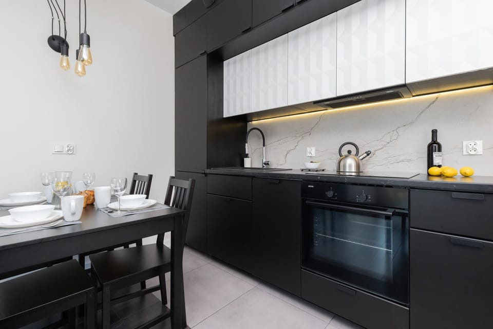 A sleek kitchen with black cabinetry, a built-in oven, and a marble backsplash, emphasizing its stylish design.