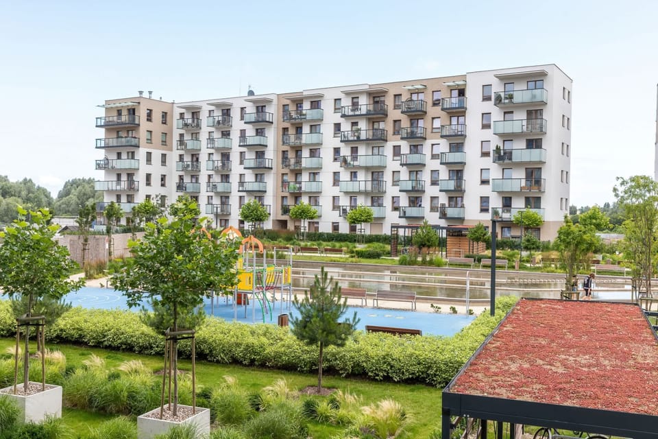 A bright outdoor view showing the apartment building surrounded by greenery and pathways.