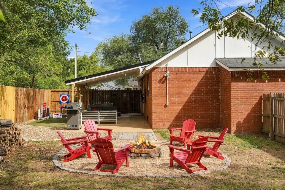 Outdoor fire pit area with red Adirondack chairs, grill, and fenced yard.