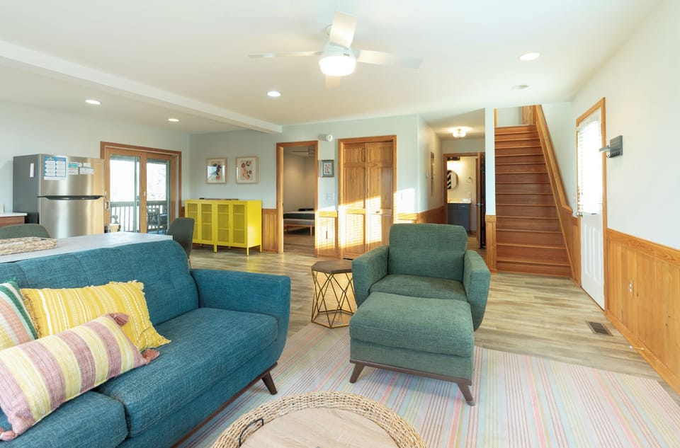 Relax in your spacious living area with plush teal seating, colorful accents, and warm wood touches throughout this bright, open-concept space.