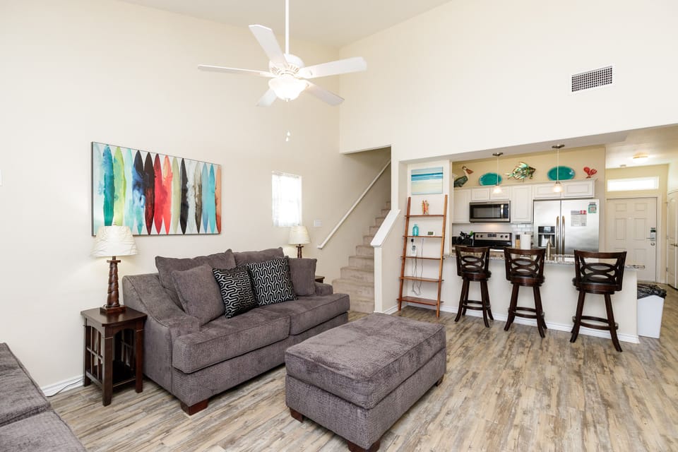 Relax in your spacious living room with cozy gray seating, modern art, and an open kitchen perfect for entertaining.