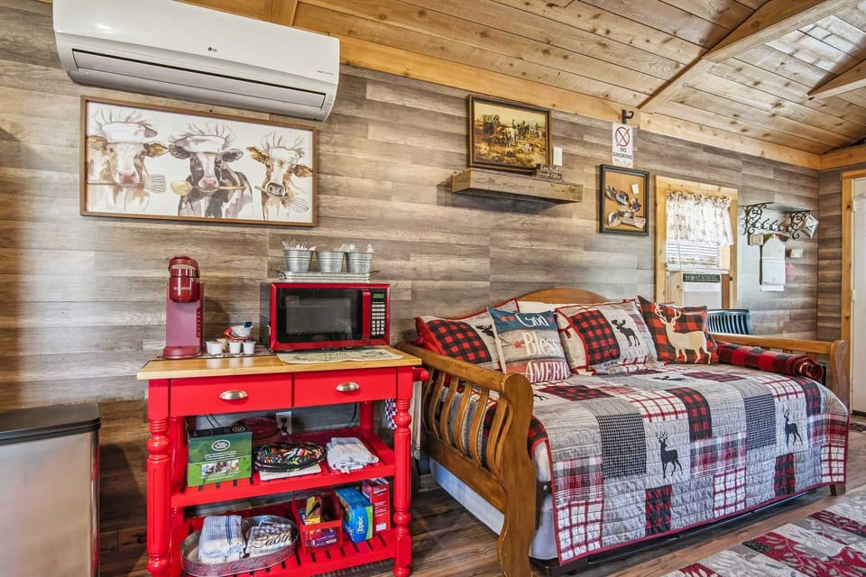 A cozy corner of the cabin featuring a bright red kitchen cart equipped with a microwave and coffee maker, situated next to a rustic wooden daybed with lodge-inspired patchwork bedding.