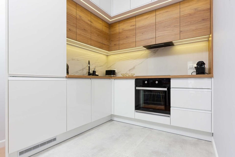 A sleek kitchen with white cabinets and wooden accents. Features built-in appliances and contemporary lighting.

