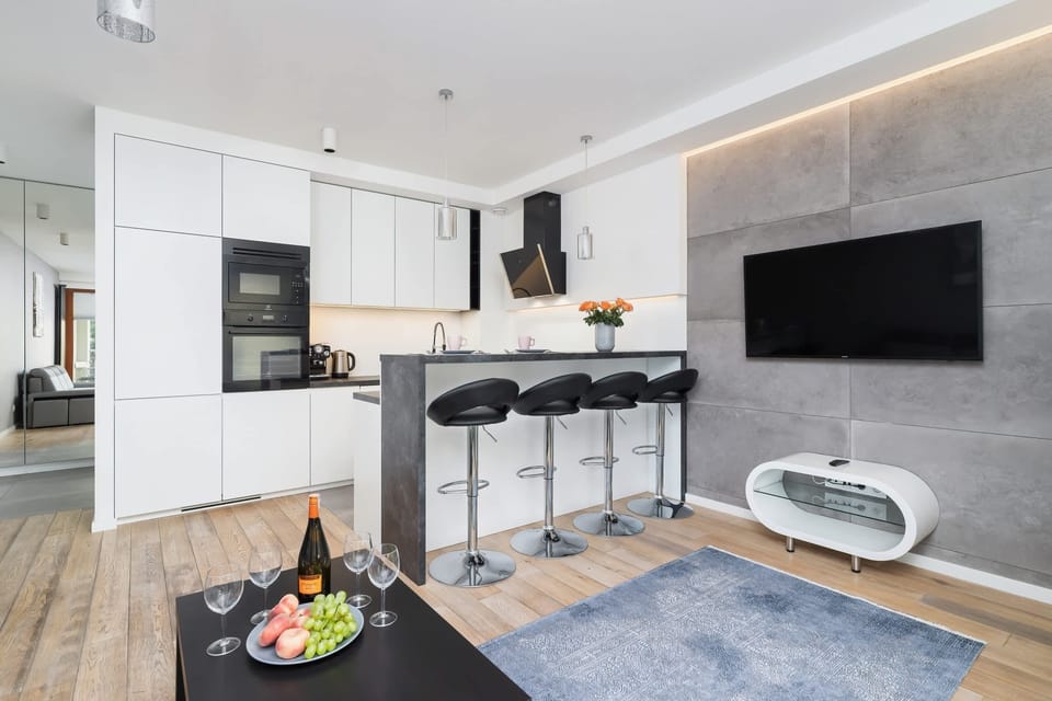 A spacious living area with a modern kitchen, stylish bar stools, and a large TV setup, designed for comfort and functionality.