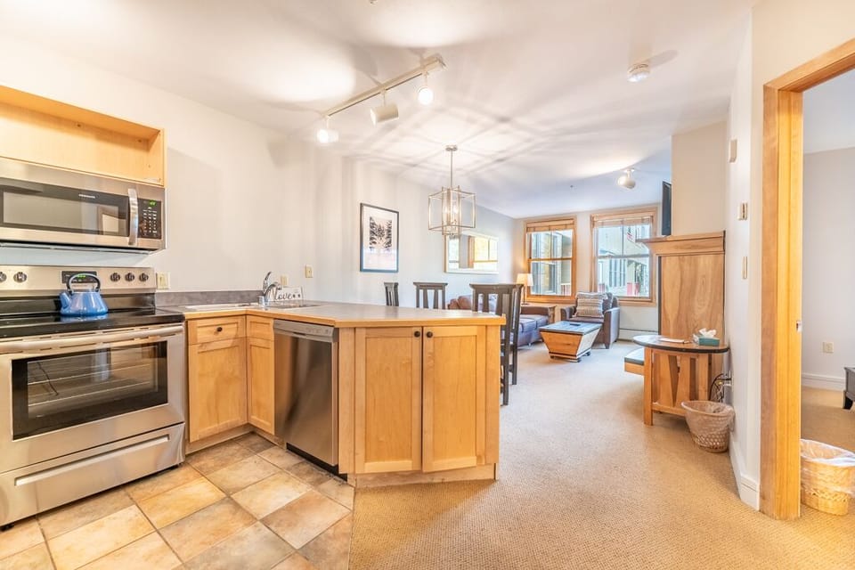 Your open-plan kitchen flows seamlessly into the cozy living area, featuring warm wood cabinetry and stainless appliances perfect for preparing meals together.