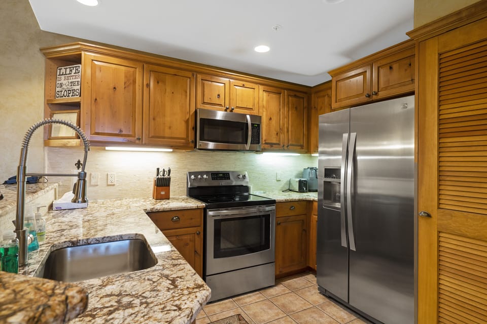 A modern kitchen with stainless steel appliances, wooden cabinets, granite countertops, and a double sink.