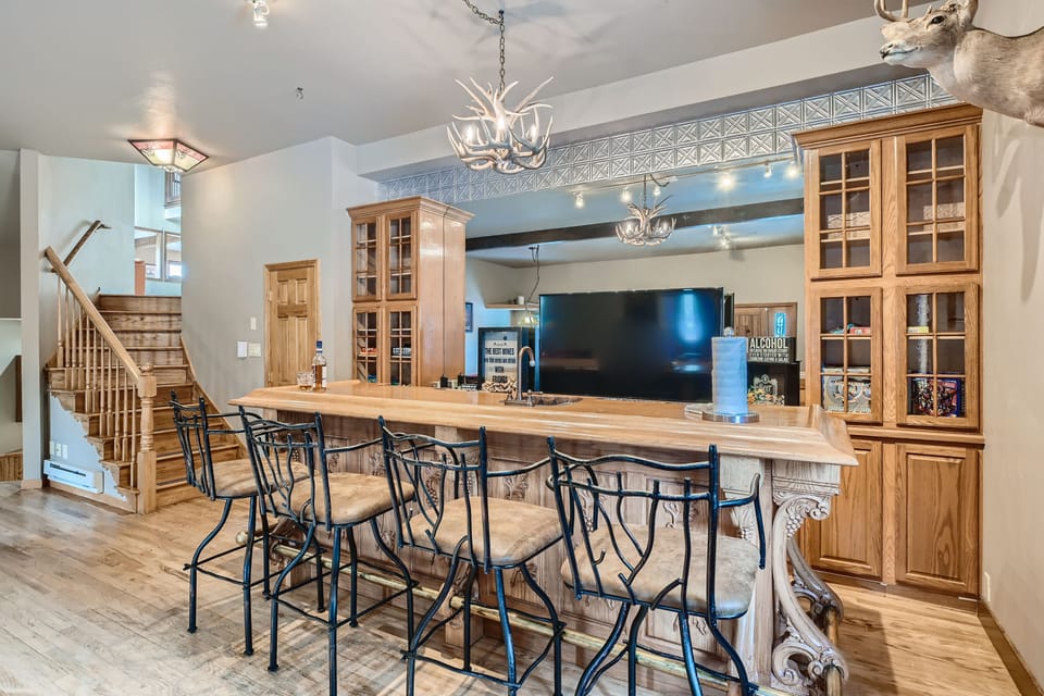 Kitchen with a wooden island, four bar stools, and glass-front cabinets, featuring antler chandeliers and a mounted deer head on the wall.