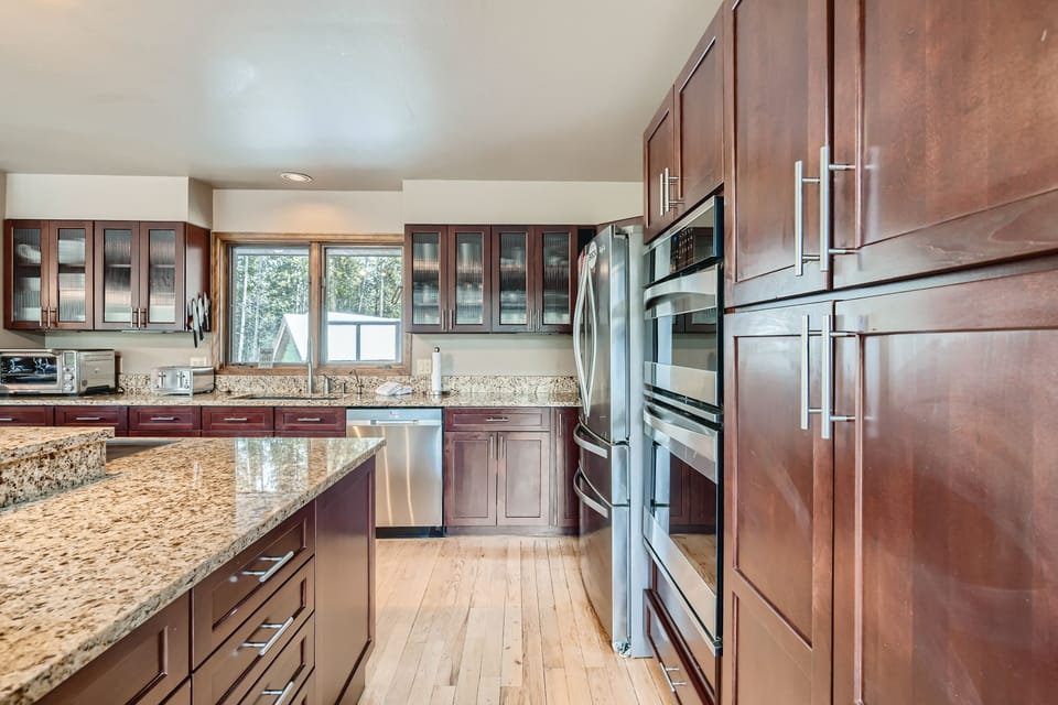 Modern kitchen with wooden cabinets, stainless steel appliances, granite countertops, and large windows.