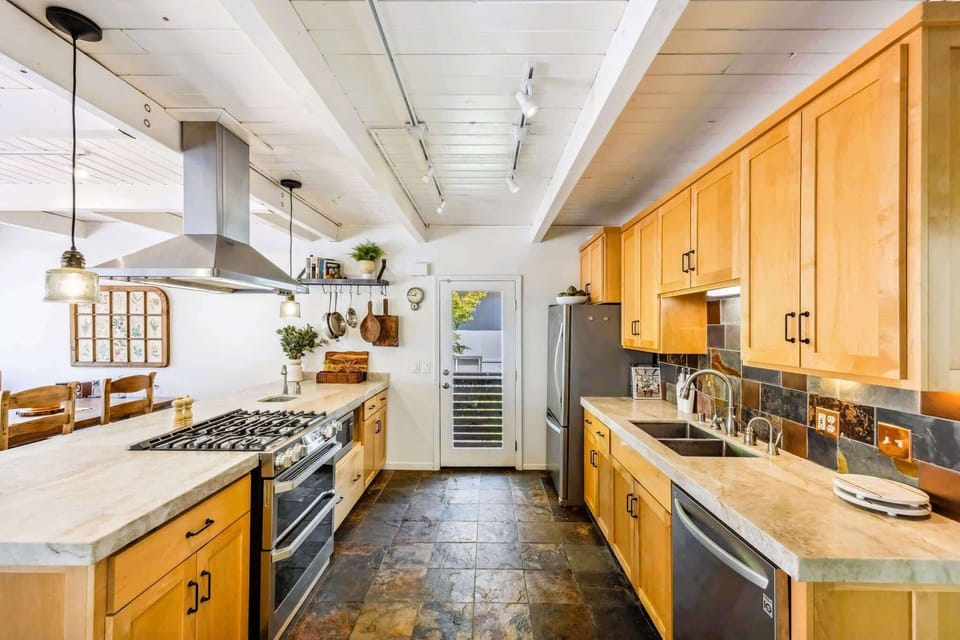 Spacious chef’s kitchen with gas range, marble countertops, modern appliances, and warm wood cabinetry—perfect for cooking and entertaining.
