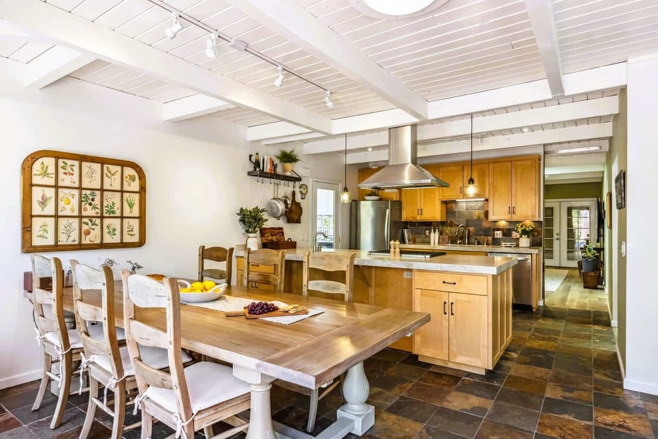 Inviting dining area beside a chef’s kitchen, featuring a farmhouse table, warm wood finishes, and an open, social layout.
