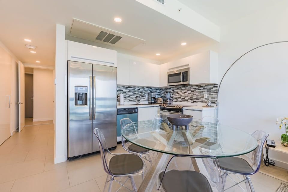 Step into a bright, modern kitchen with sleek stainless steel appliances and a stylish glass dining table—perfect for enjoying your morning coffee or prepping delicious meals during your stay.