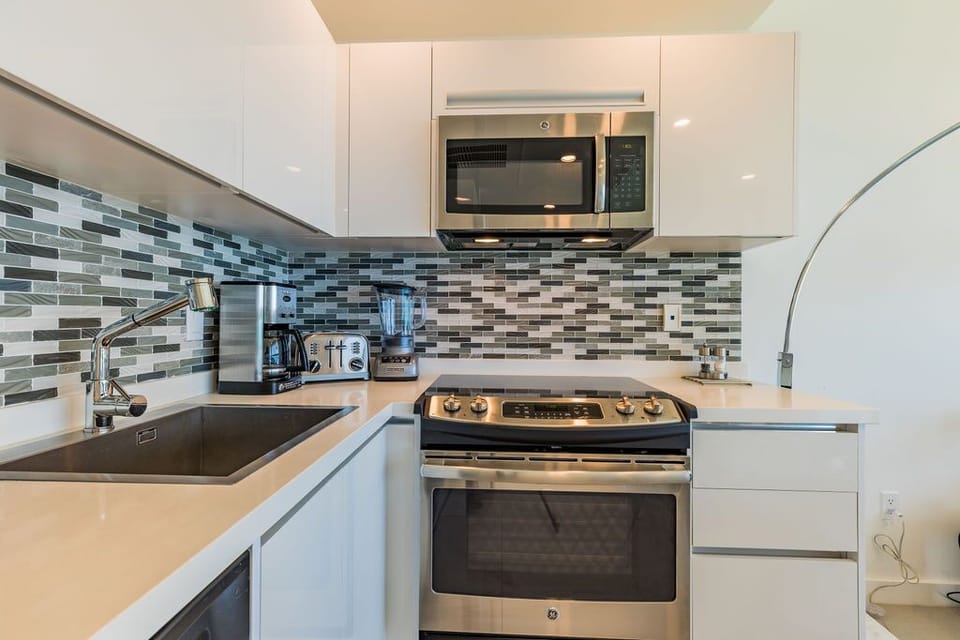 Prepare your favorite meals in this sleek, modern kitchen featuring stainless steel appliances, chic glass tile backsplash, and everything you need for easy cooking.