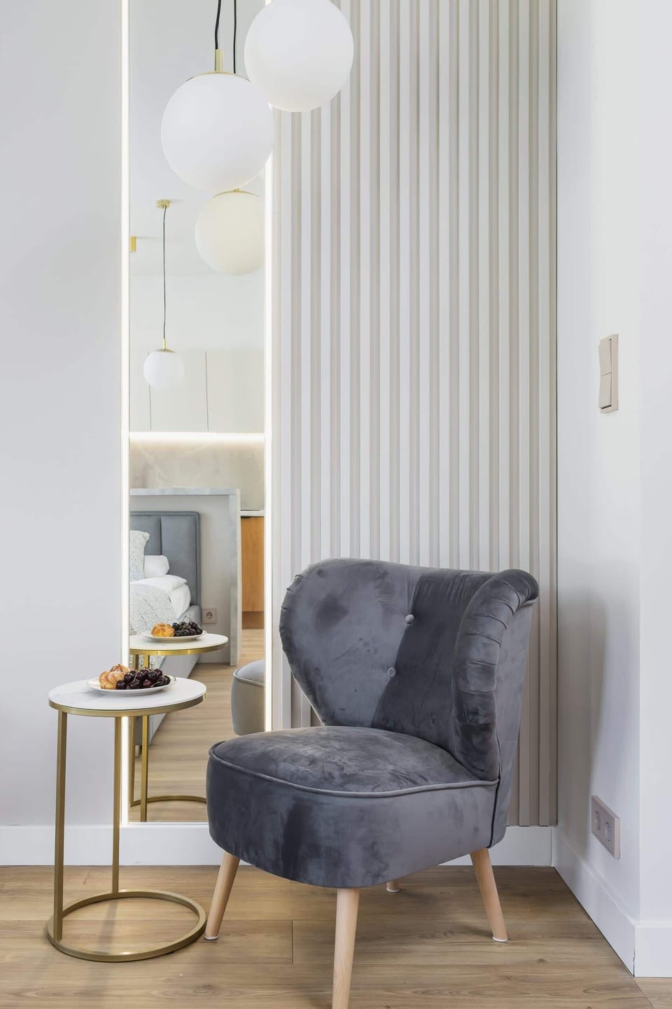 A cozy reading nook with a stylish gray armchair and a minimalist floor lamp, set against a light wall.