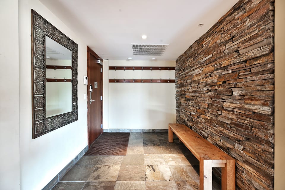 Entryway with two coat racks, wooden bench, slate stone tile floor and wall