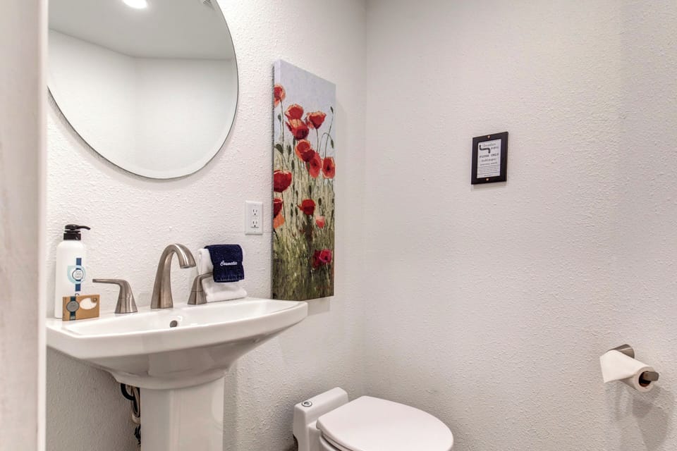 The half bathroom offers a pedestal sink and round mirror.