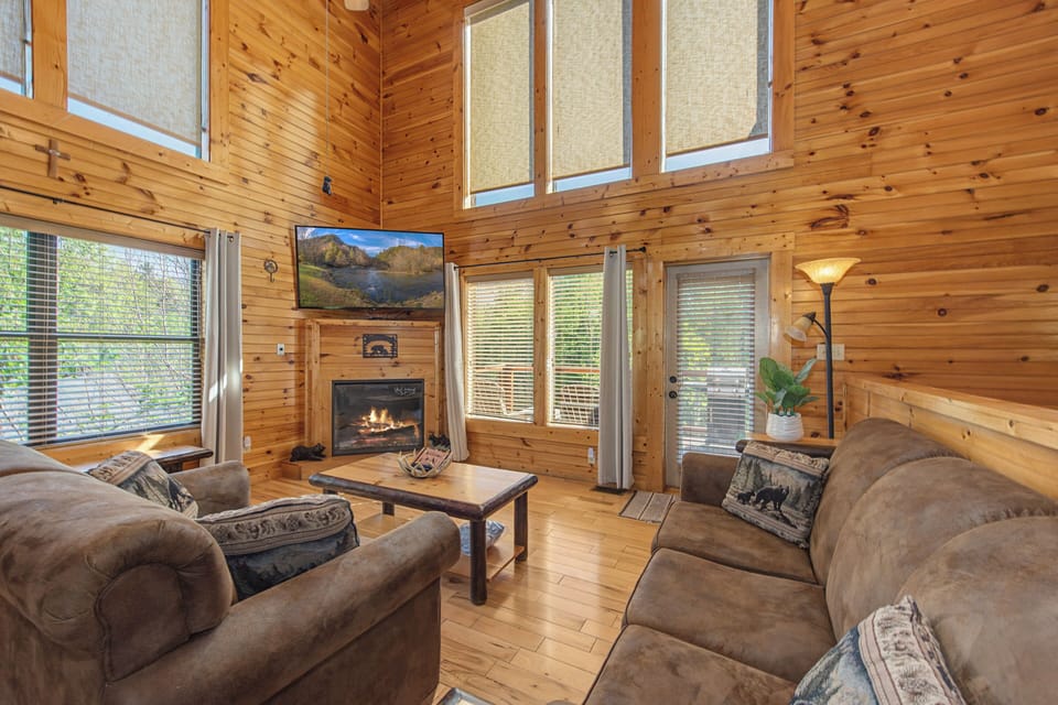 Settle into your cozy cabin living room with warm wood walls,fireplace, and plush seating perfect for mountain getaway relaxation.