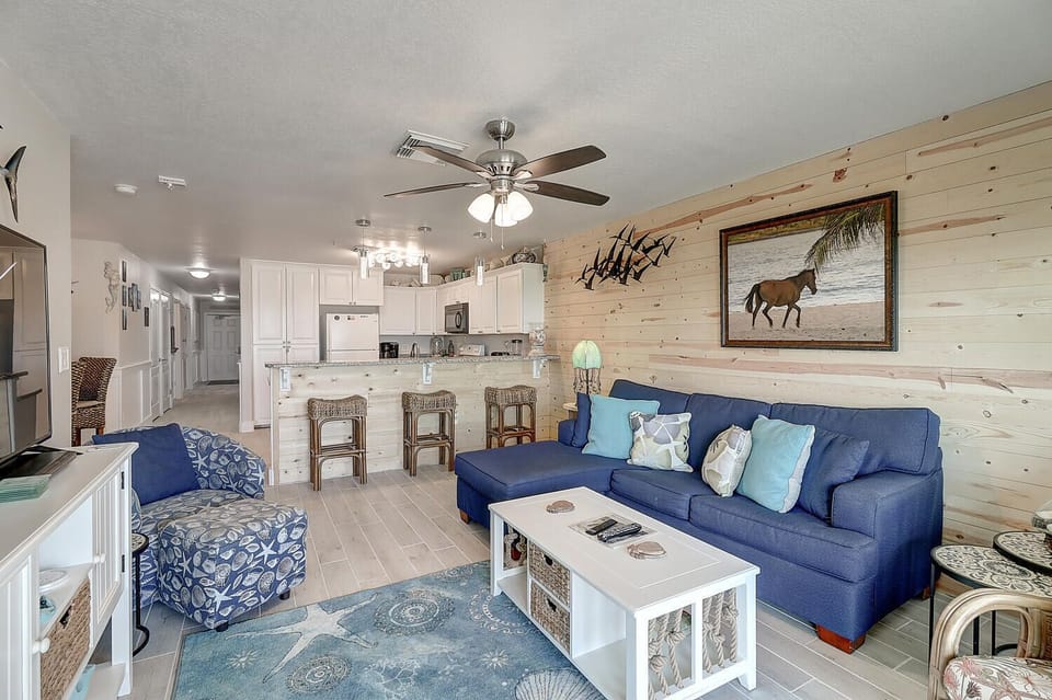 Relax on your comfortable blue sofa while enjoying the rustic wood accent wall and open kitchen in this coastal-themed space.