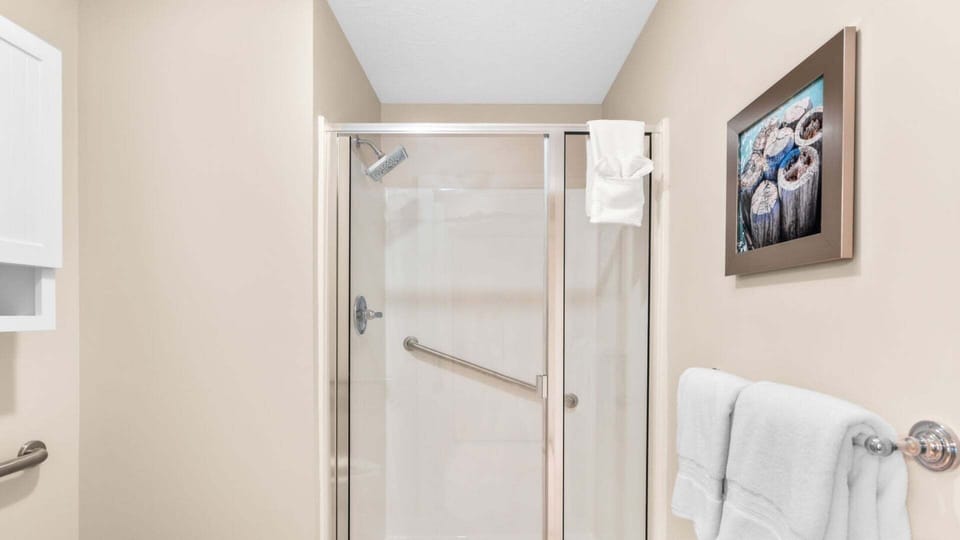 Glass-enclosed white shower with a grab bar beside neatly hung white towels.