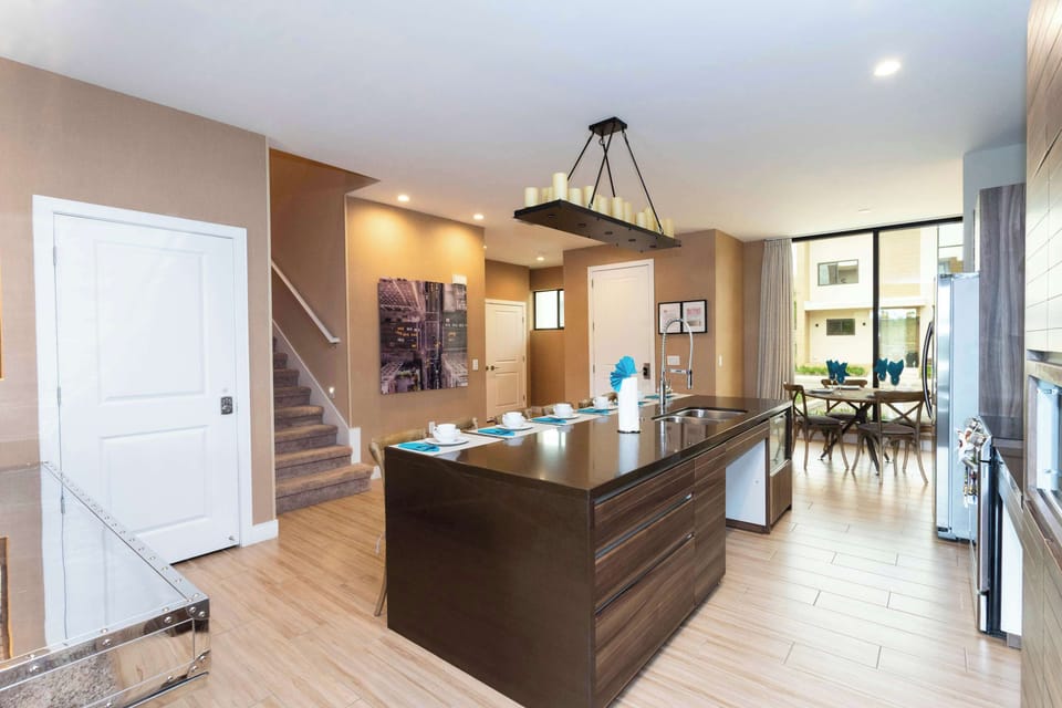 Open-plan kitchen with a glossy island, pull-down faucet, and bar seating for 6-warm wood tones and a candlelight pendant set the scene for family meals.