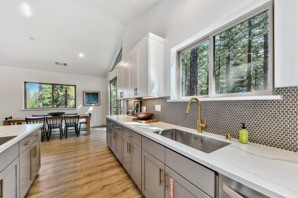 White quartz countertops and gray cabinetry line the kitchen with a brass faucet and hexagonal tile backsplash.