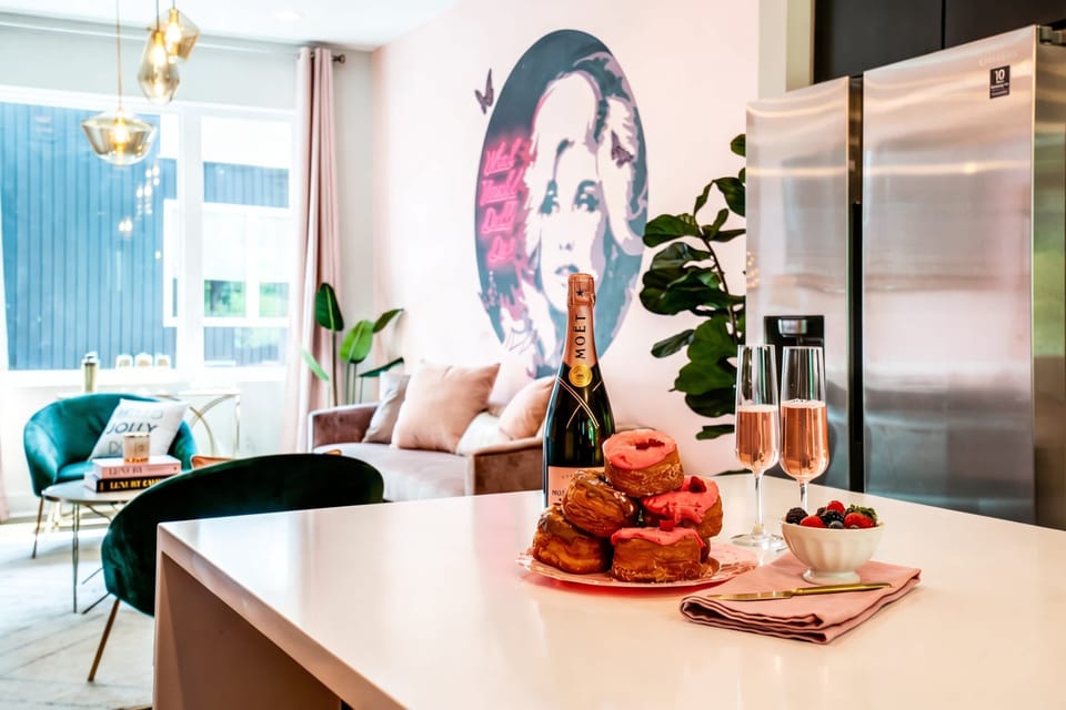 The kitchen opens to living space where a Dolly mural sets the tone: champagne, donuts, and 12 people all in one frame to start the day