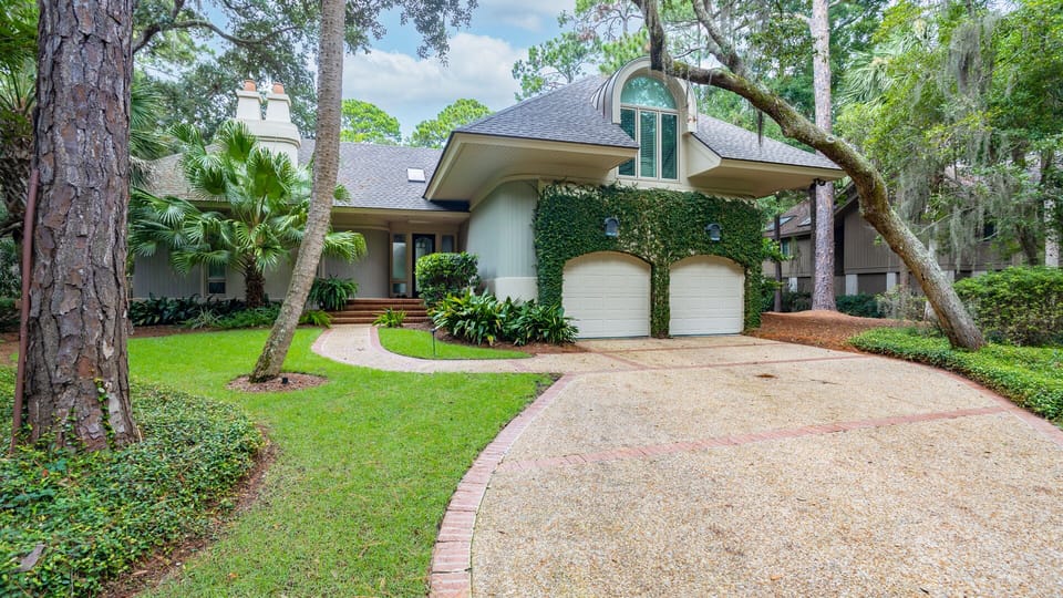 The curved driveway leads to a charming façade featuring a vine-covered exterior, arched architectural details, and a two-car garage.