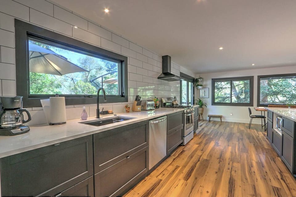 Open concept chef`s kitchen with large windows overlooking trees & deck