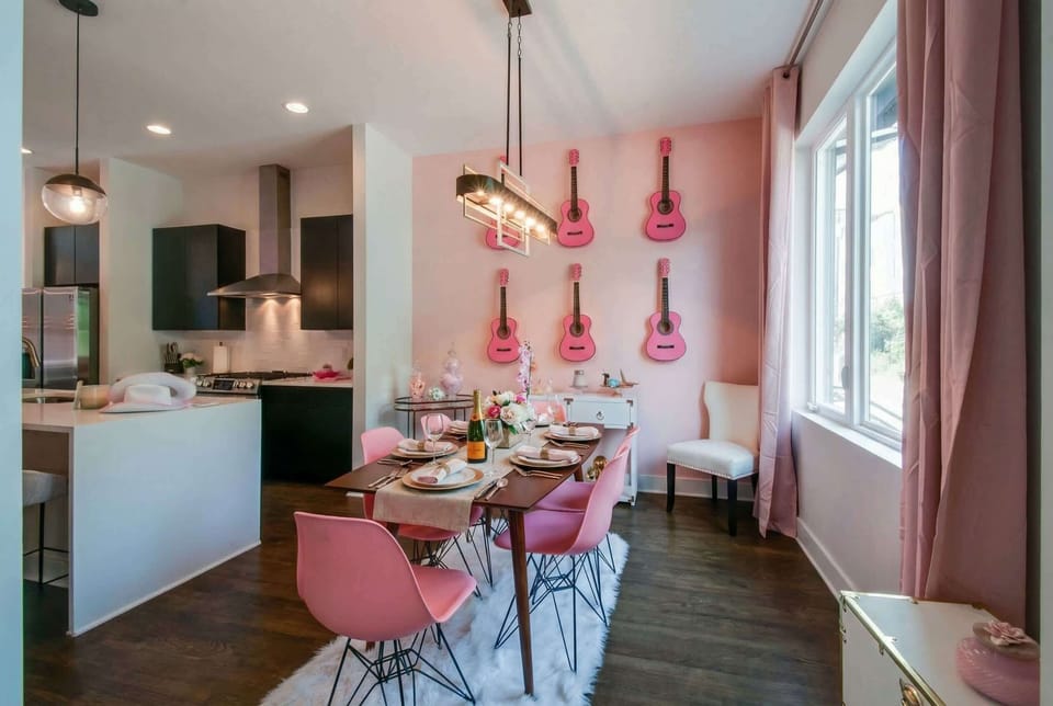 Pink guitars hang above the dining table in the Dolly-inspired home, where pink chairs and open sightlines to the kitchen keep the vibe warm and connected