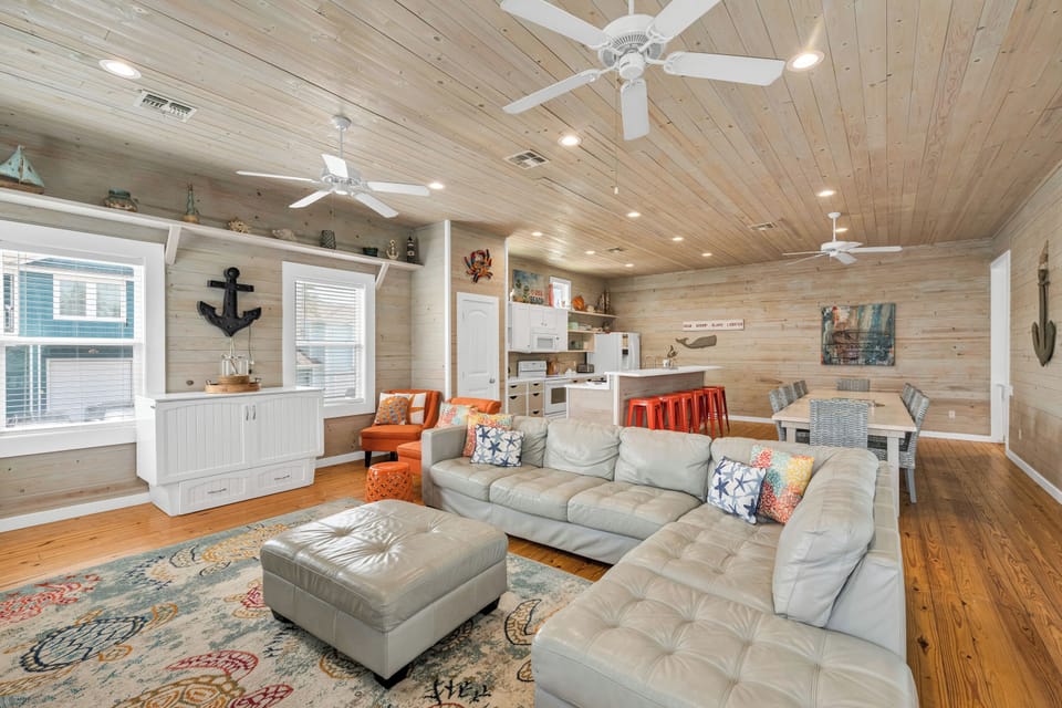 Relax in your spacious open-plan living area with plush sectional seating, coastal decor, and exposed wood ceilings that create a warm, beachy atmosphere.