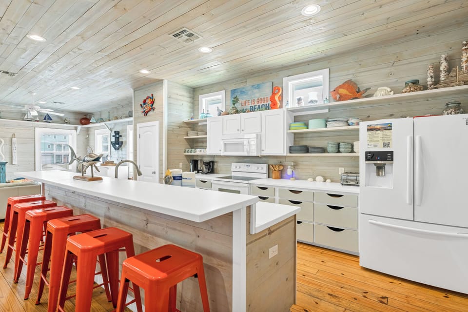 Your bright coastal kitchen features weathered wood, white quartz counters, and cheerful orange stools perfect for morning coffee.