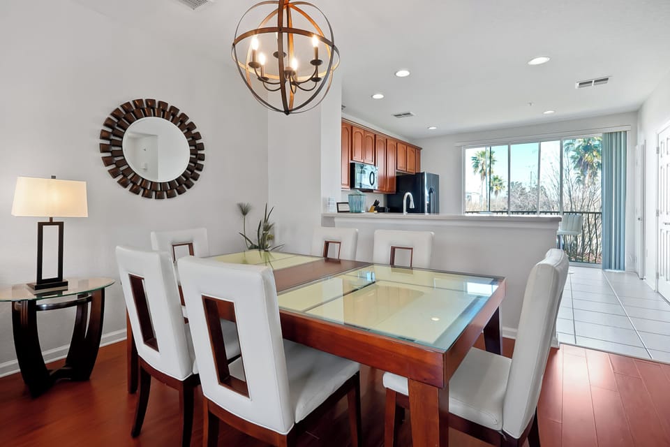 Gather around your elegant dining table with gleaming glass top, surrounded by plush white chairs under stunning chandelier light.
